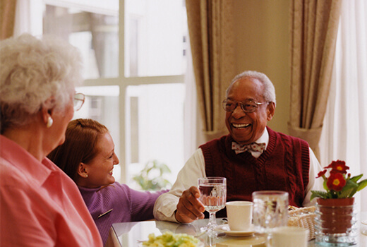Two residents and a staff member smiling at a dinner table